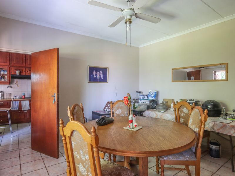 Open plan dining area featuring tiled flooring and a ceiling fan, with an adjacent kitchen showcasing traditional wooden cabinetry and tiled backsplash.