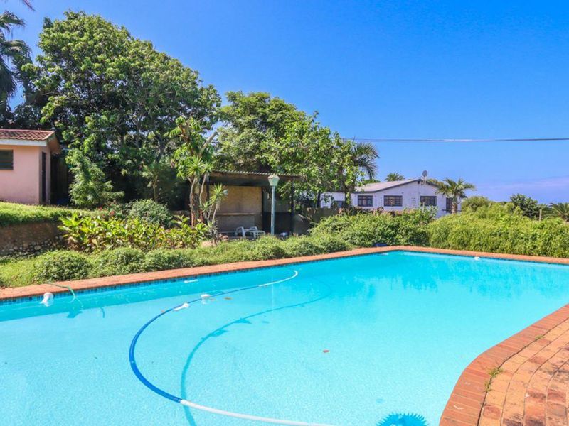 Outdoor pool area featuring a swimming pool with brick coping, surrounded by a landscaped garden and a covered entertainment structure.