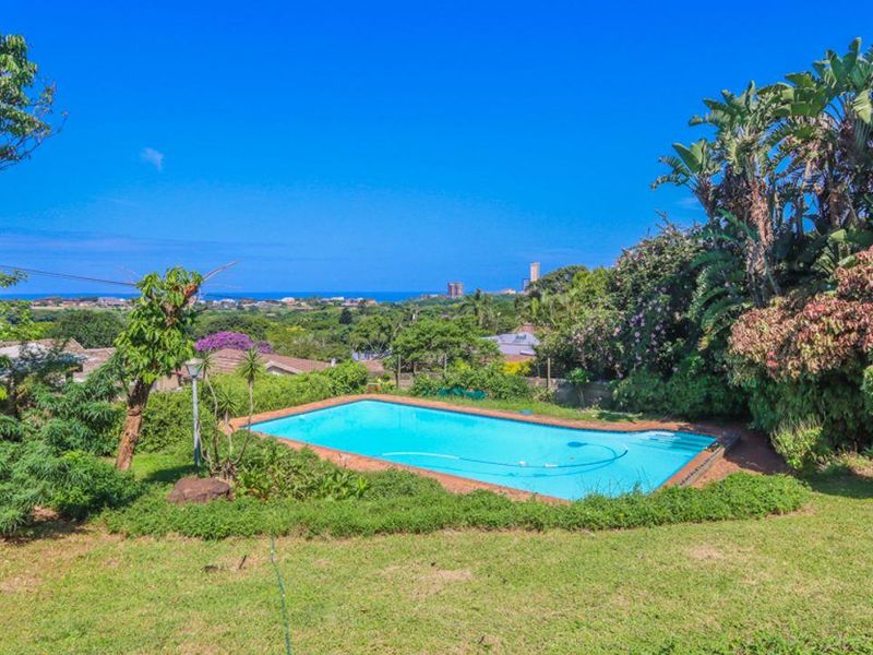 A well-maintained swimming pool set within a lush garden, offering expansive views of the surrounding landscape and distant coastline.