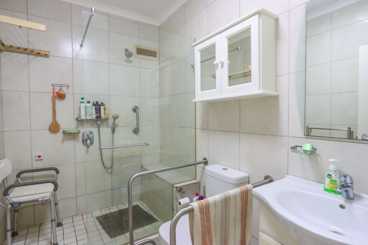Functional bathroom featuring a walk-in shower with glass screen, grab rails, wall-mounted vanity cabinet, and a pedestal basin.