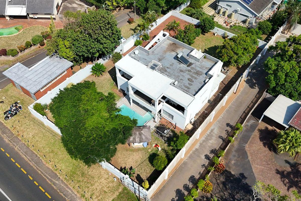Aerial view of a multi-level residential property featuring a flat roof, private swimming pool, and established garden within a suburban setting.