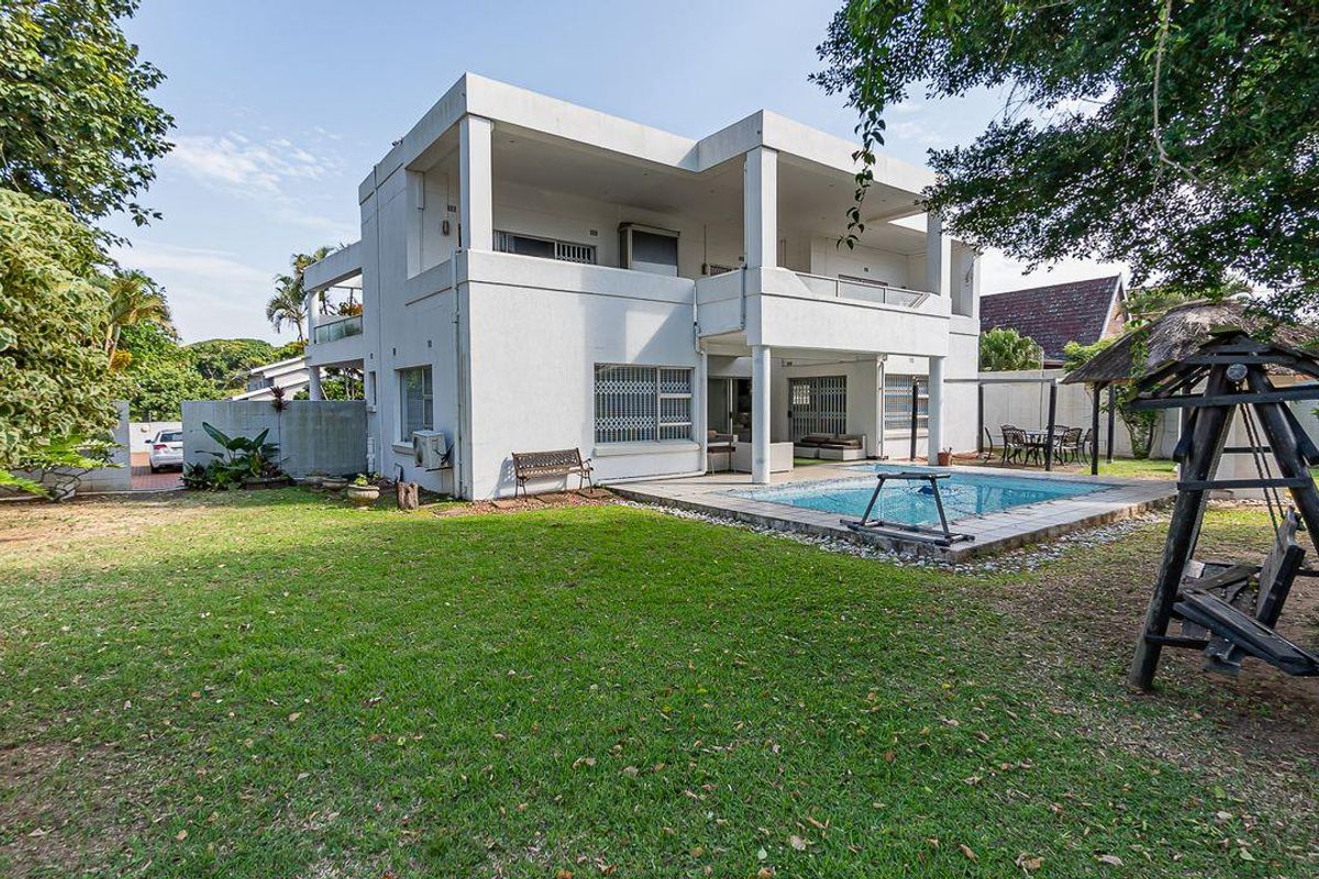 Rear view of a multi-story house featuring a swimming pool, covered patio areas, and a spacious garden.