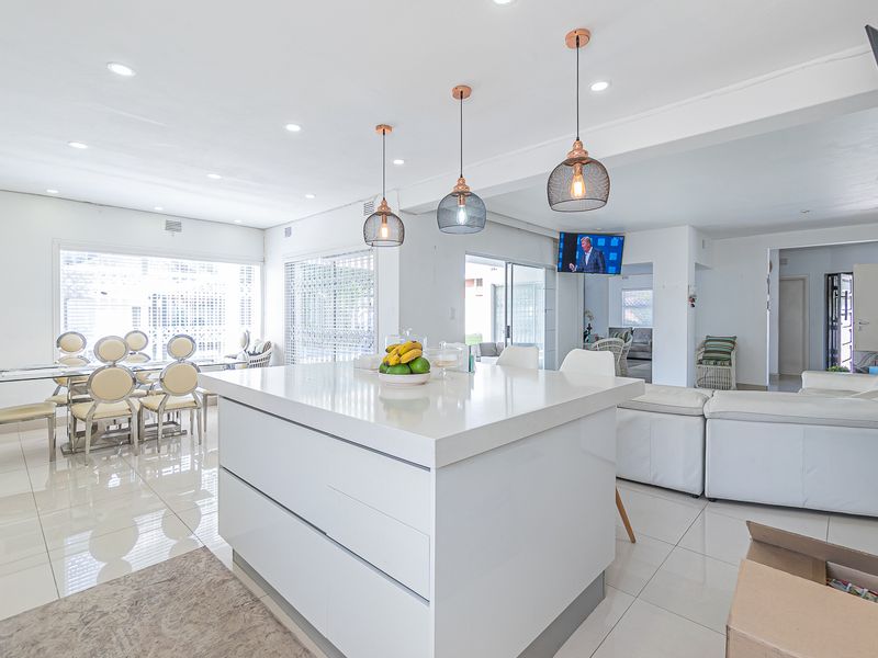 Open-plan living and dining area featuring a central kitchen island with pendant lighting and polished floor tiles throughout.