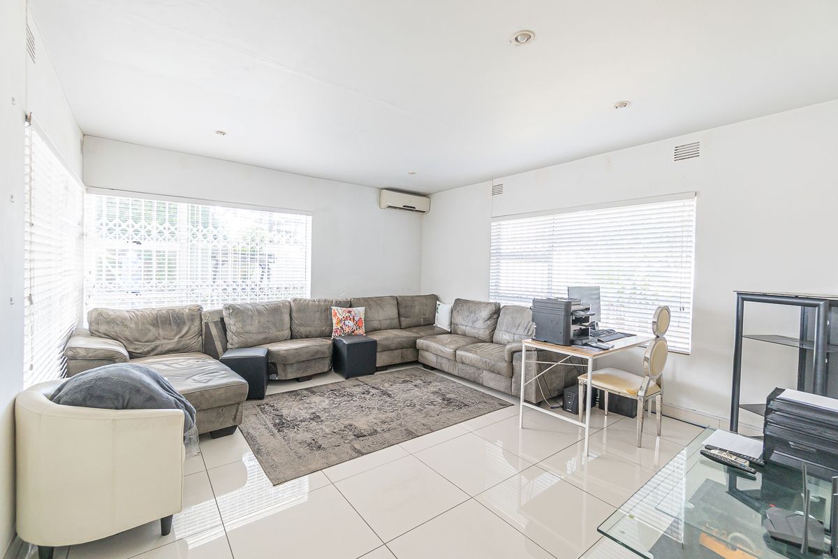 Spacious living room featuring large format floor tiles, recessed downlighting, and wall-mounted air conditioning unit with ample natural light from multiple windows.
