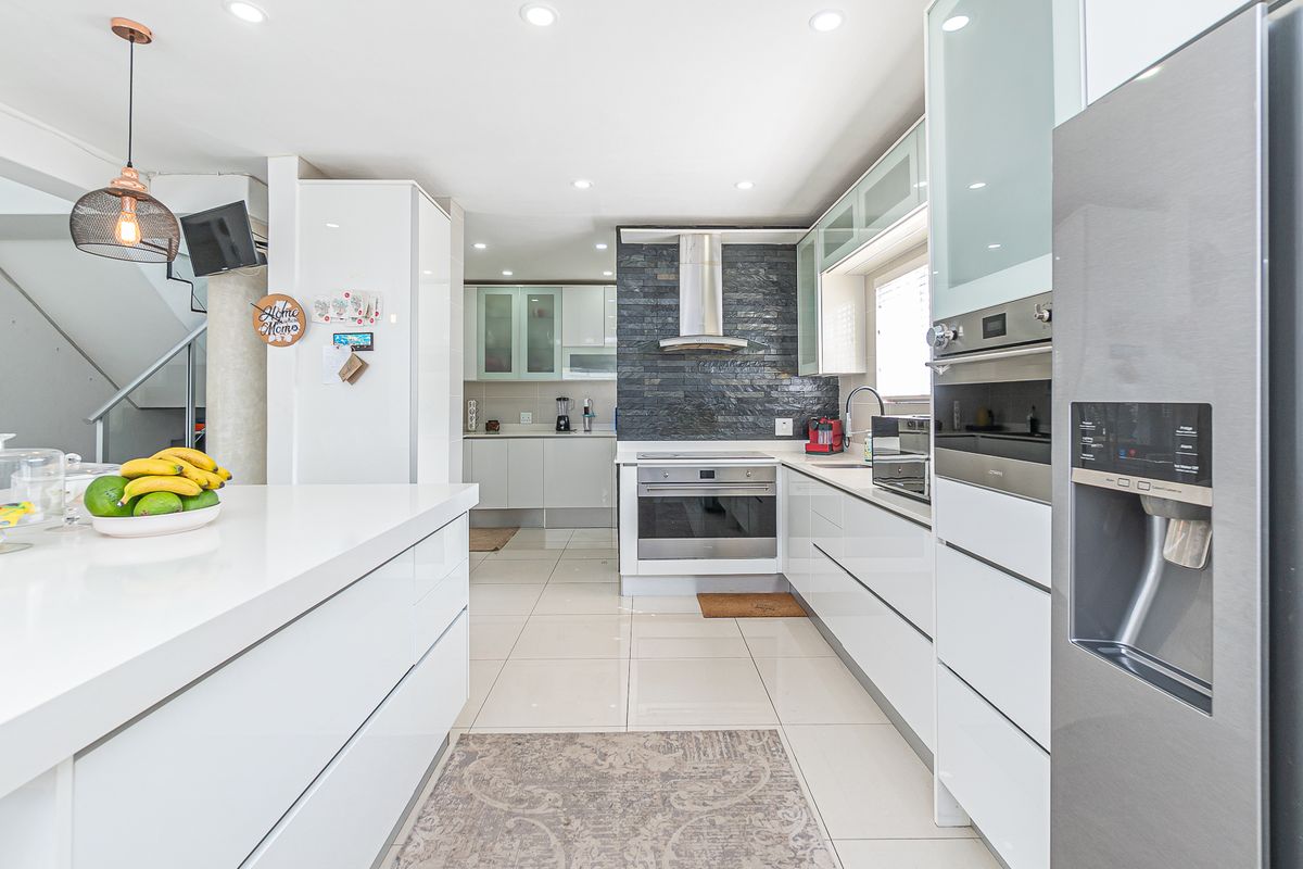 Modern kitchen featuring high-gloss cabinetry, stone countertops, a built-in oven, extractor fan, and a striking dark stone feature wall.