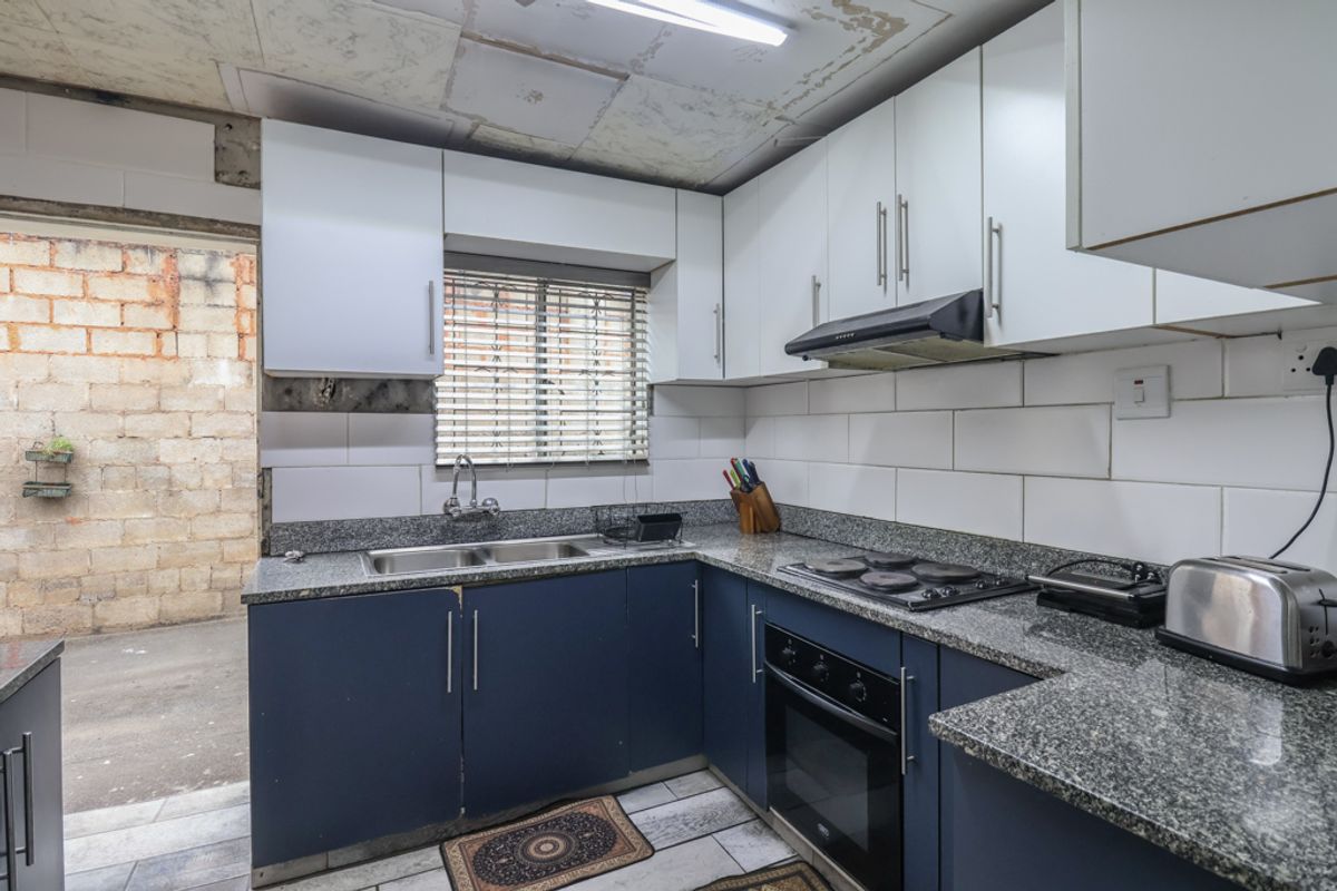 Compact kitchen featuring granite countertops, built-in oven, and hob. The space requires ceiling repairs and finishing touches to complete the aesthetic.