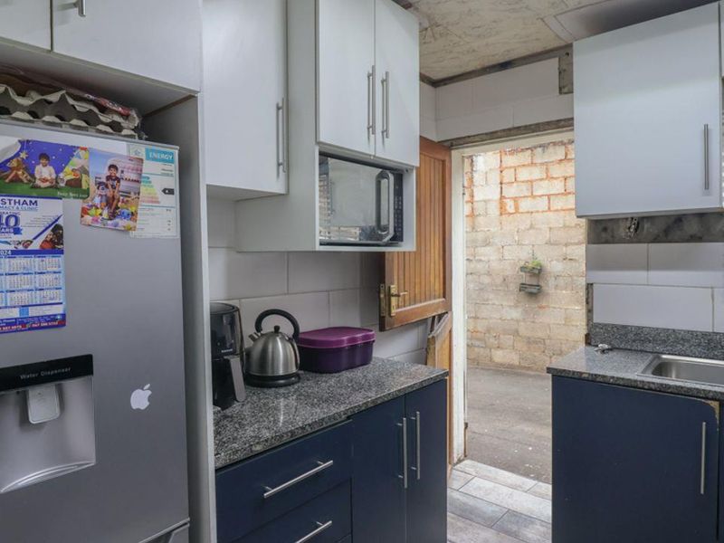 Compact kitchen featuring dark blue base cabinets, white wall units, granite countertops, and a stainless steel sink, with direct access to an exterior area.