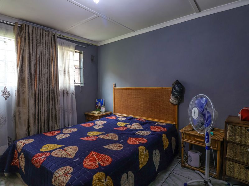 A functional bedroom featuring tiled flooring, security bars on the windows, and a neutral wall finish, offering a comfortable and practical living space.