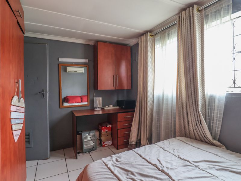 A functional bedroom featuring built-in cabinetry, tiled flooring, and security bars on the windows, providing a practical living space.