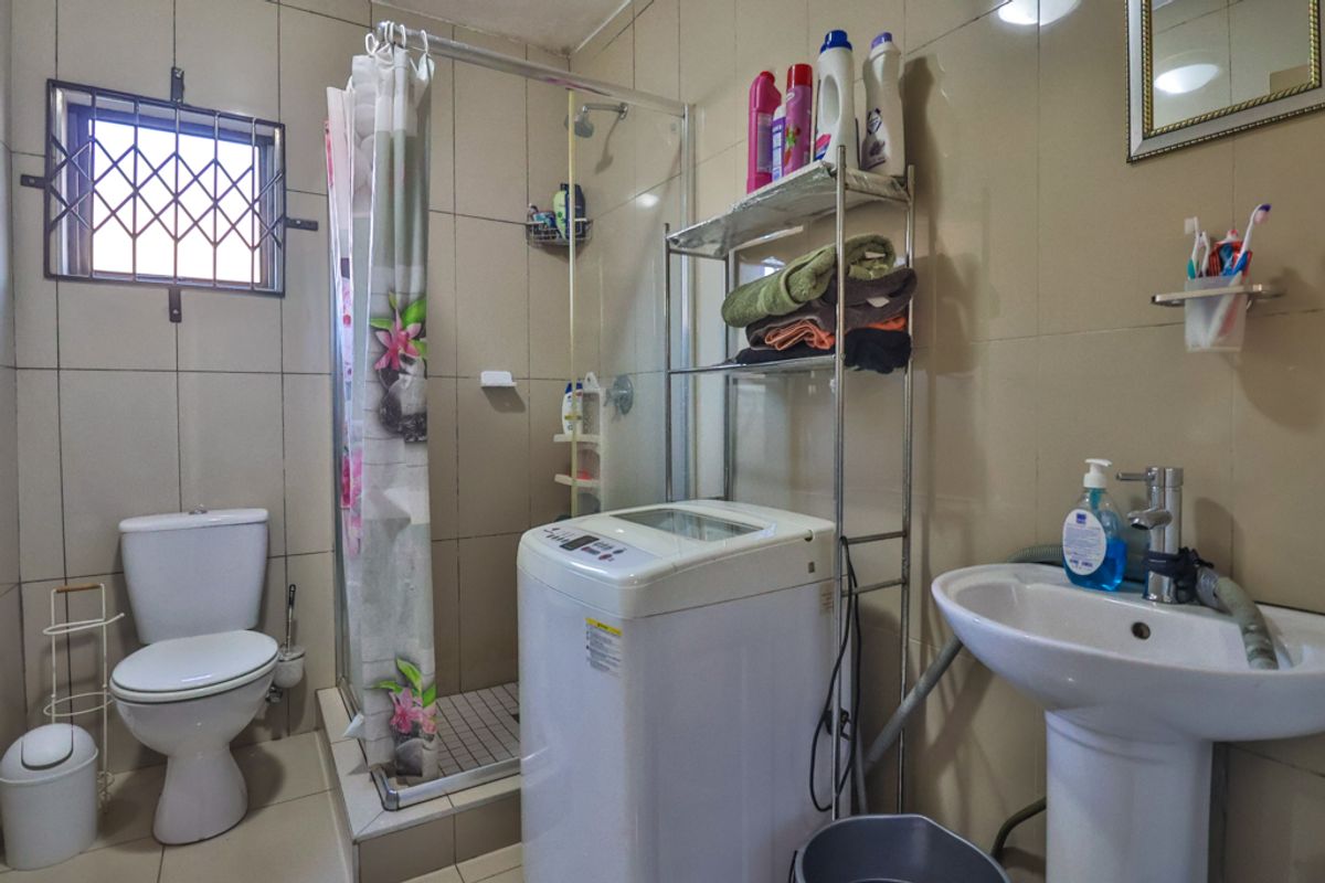A functional bathroom featuring a shower enclosure, pedestal basin, and toilet, with integrated space for laundry appliances.