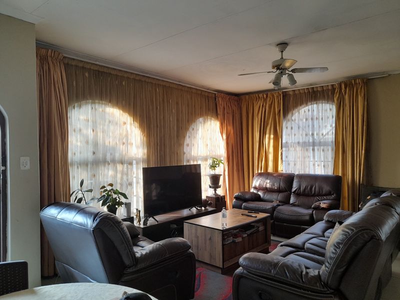 A living room featuring arched windows with floor-to-ceiling curtains and a central ceiling fan.