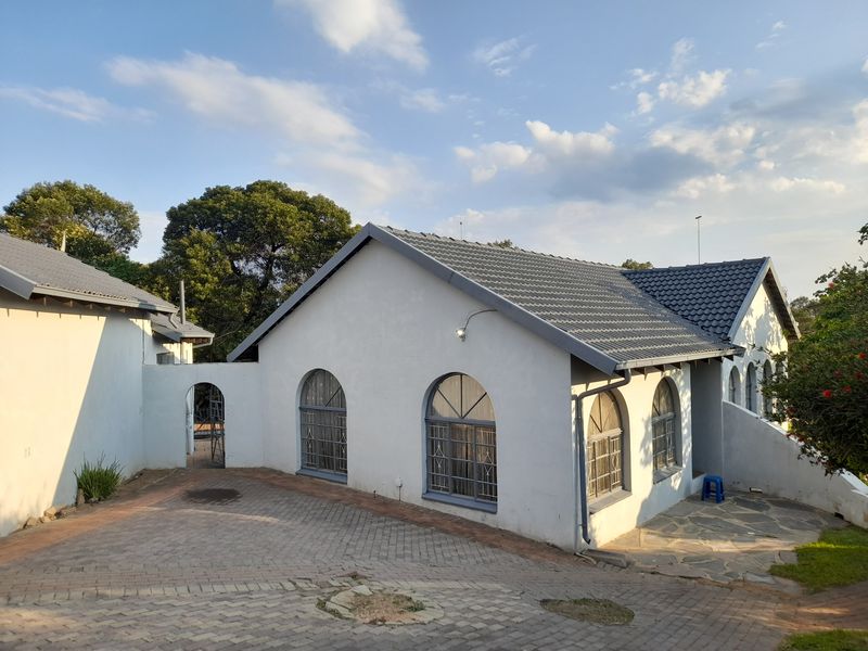 A well-maintained single-story home featuring a tiled roof, arched windows, and a paved driveway with an adjacent stone patio area.