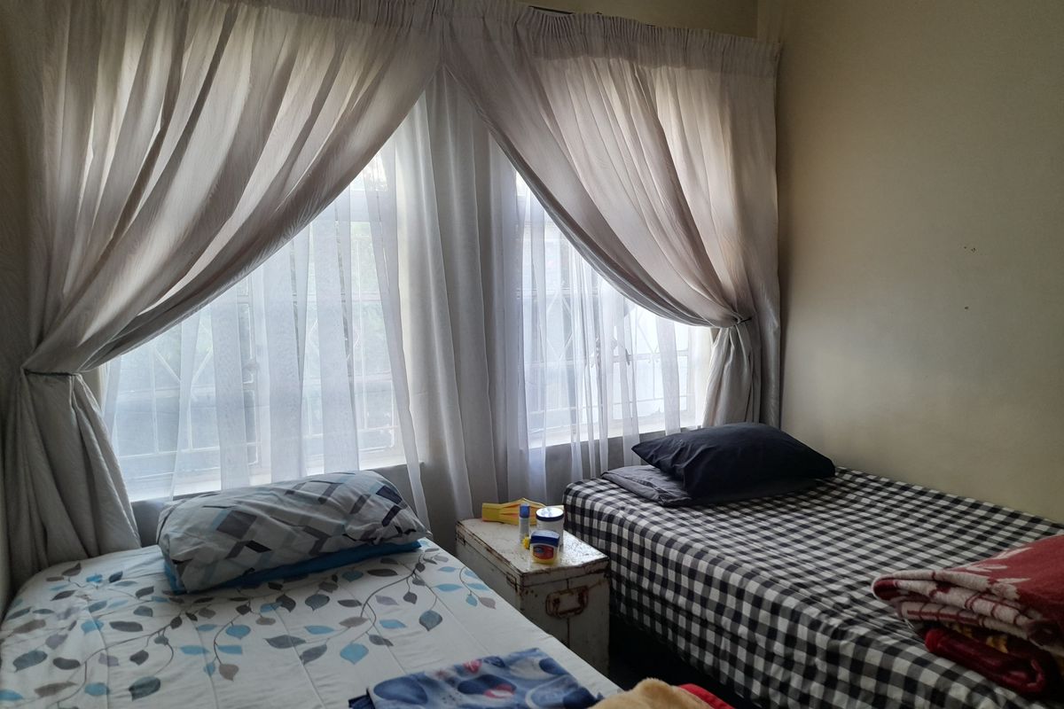 A bedroom featuring large windows with security bars and installed curtain rails, providing natural light to the space.