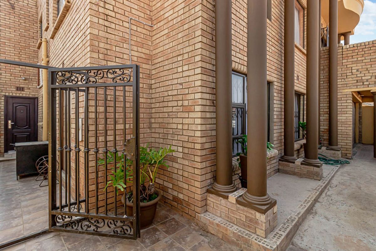 Exterior view of the property featuring a brick facade, decorative columns, and a metal security gate leading to a paved walkway.