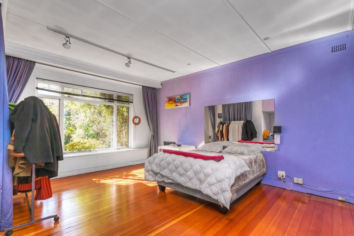 Spacious bedroom featuring polished timber flooring, large windows with natural light, and a built-in wall mirror.