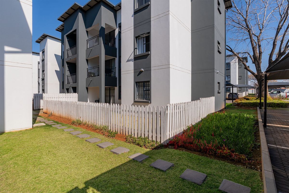 Exterior view of a modern apartment complex featuring landscaped garden areas, paved walkways, and private fenced ground-floor patio spaces.