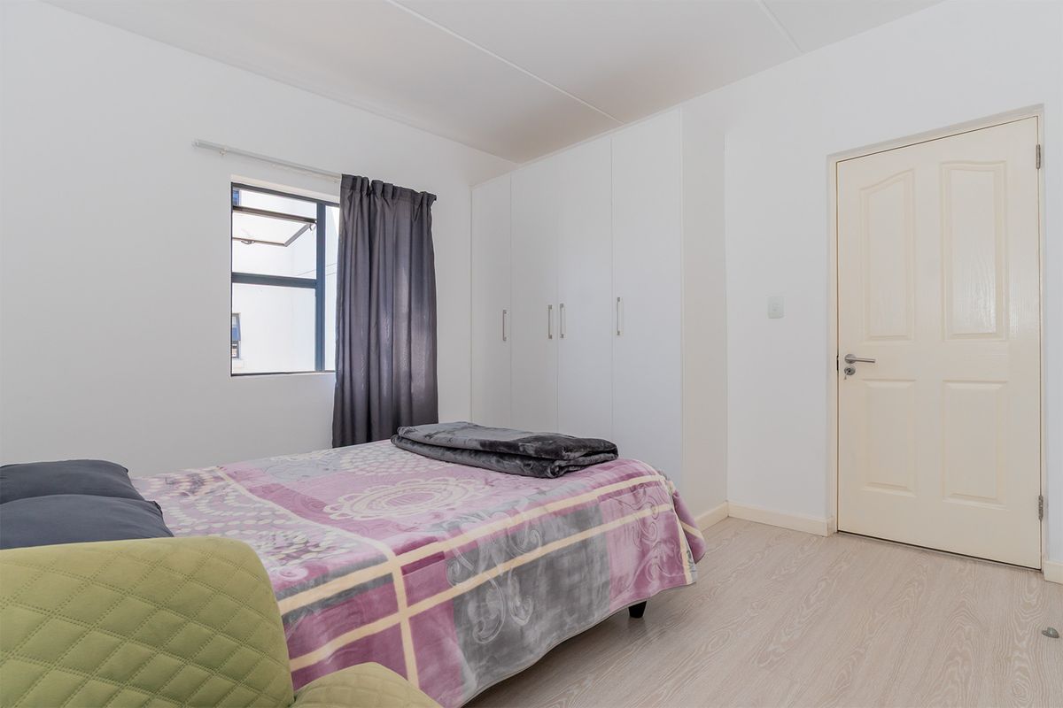 A functional bedroom featuring built-in wardrobes, light-toned laminate flooring, and a window providing natural light.
