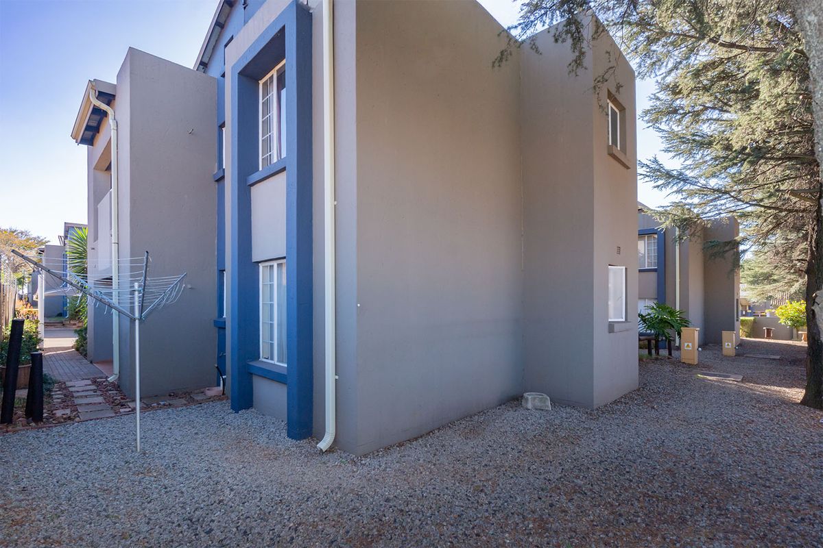 Side view of a multi-story townhouse featuring grey and blue painted exterior walls, gravel ground cover, and established trees.