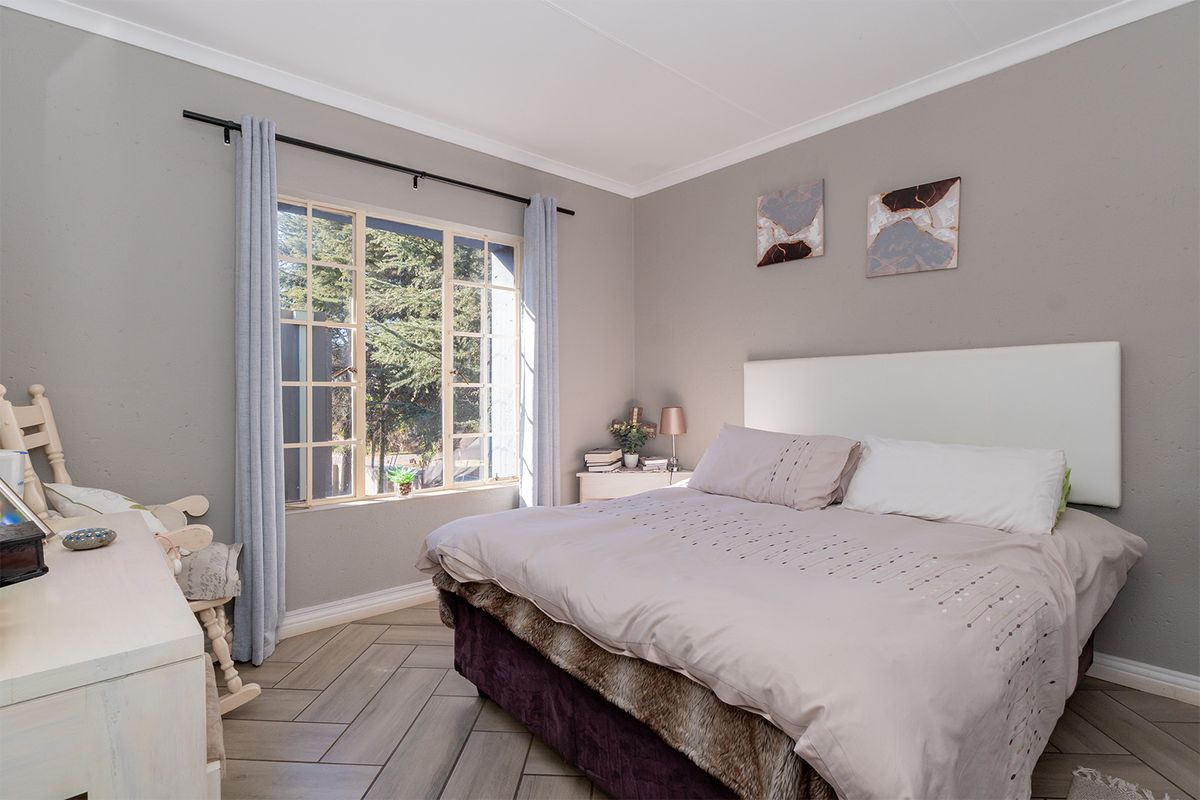 A well-maintained bedroom featuring herringbone-patterned tiled flooring, neutral wall tones, and a large window allowing for natural light.
