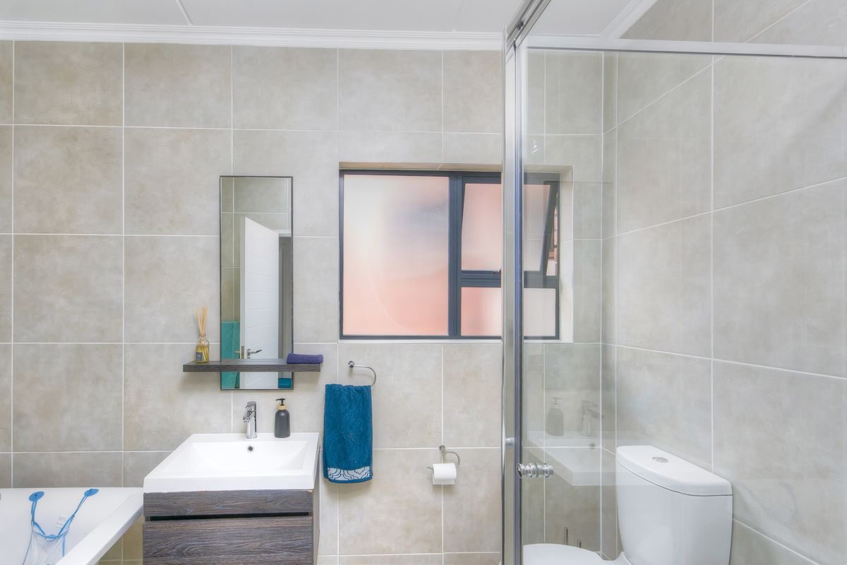 Modern bathroom featuring floor-to-ceiling neutral tiling, a floating vanity with basin, a glass-enclosed shower, and a separate bathtub.