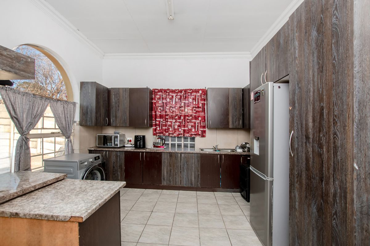 A functional kitchen featuring dark wood-look cabinetry, tiled flooring, and an arched window, providing a practical workspace with integrated storage and appliance connections.