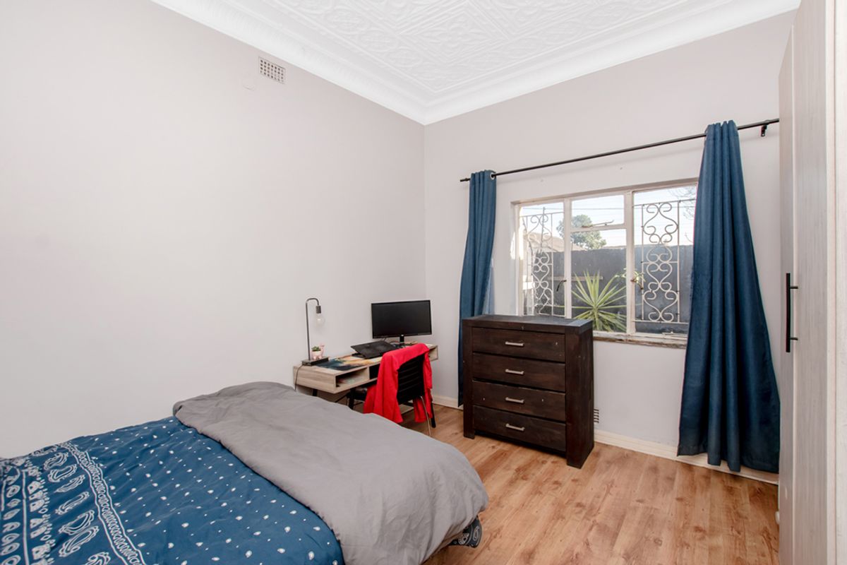 A bedroom featuring laminate flooring, decorative ceiling cornice, and a window fitted with security bars.