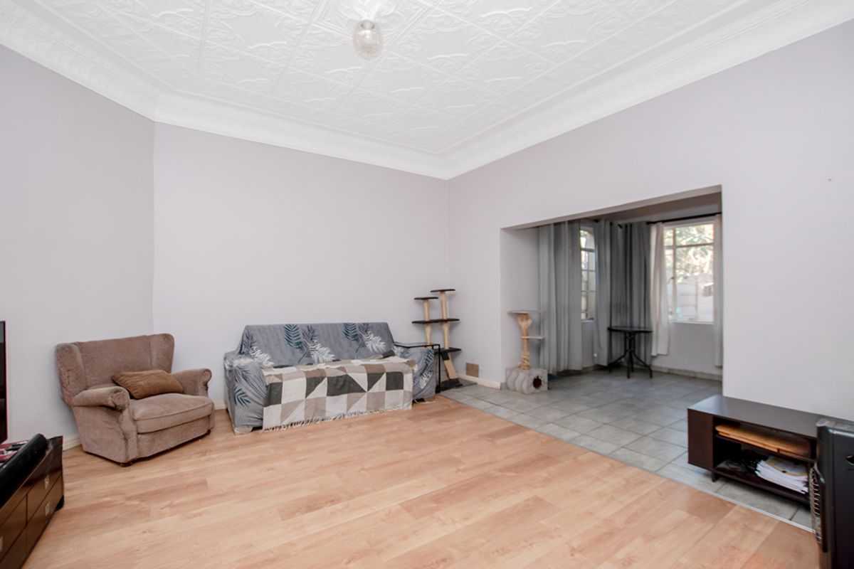 Spacious living area featuring decorative pressed metal ceilings, laminate wood flooring, and an adjoining tiled sunroom or secondary living space.
