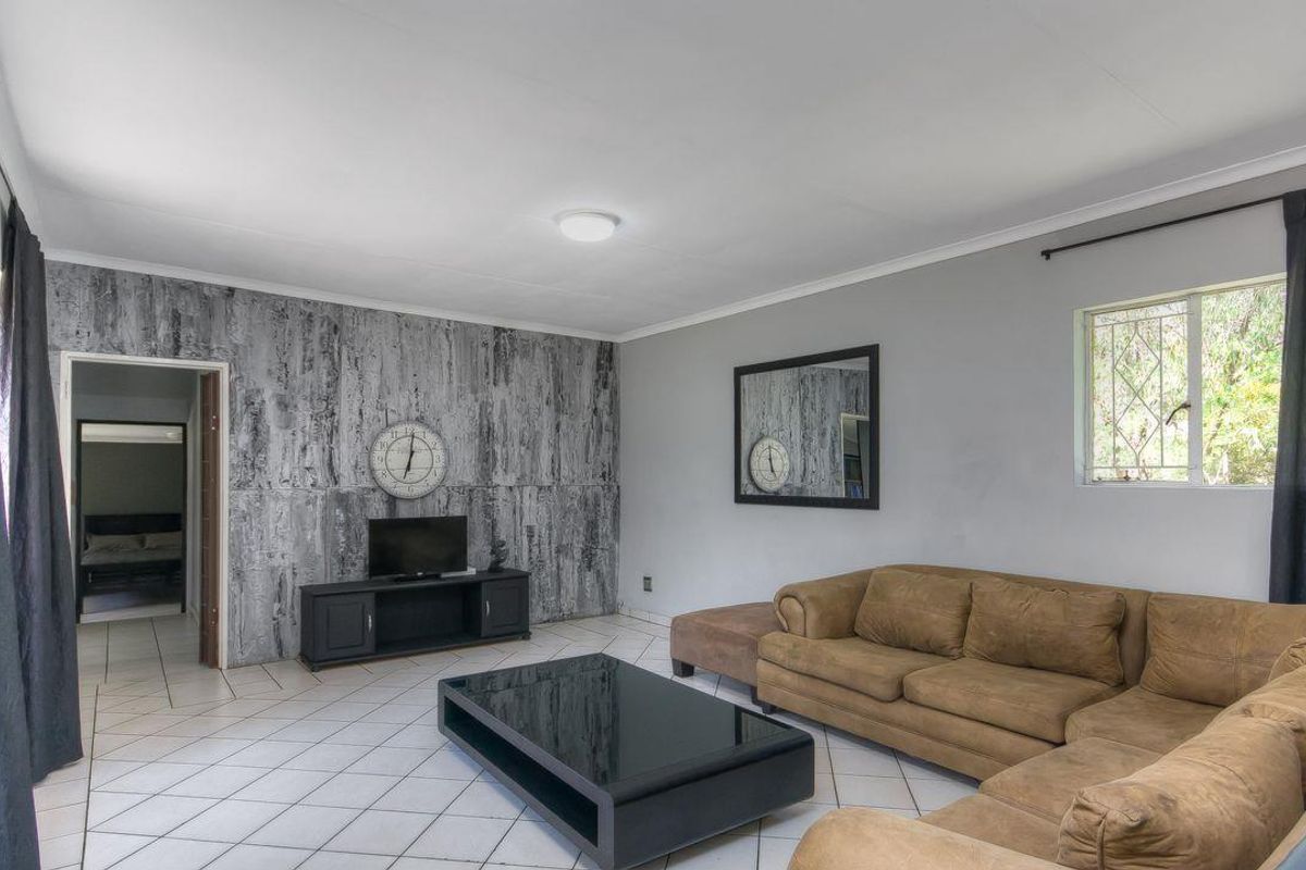 Spacious living room featuring tiled flooring, a textured feature wall, and a window with security bars, providing a functional and open living space.