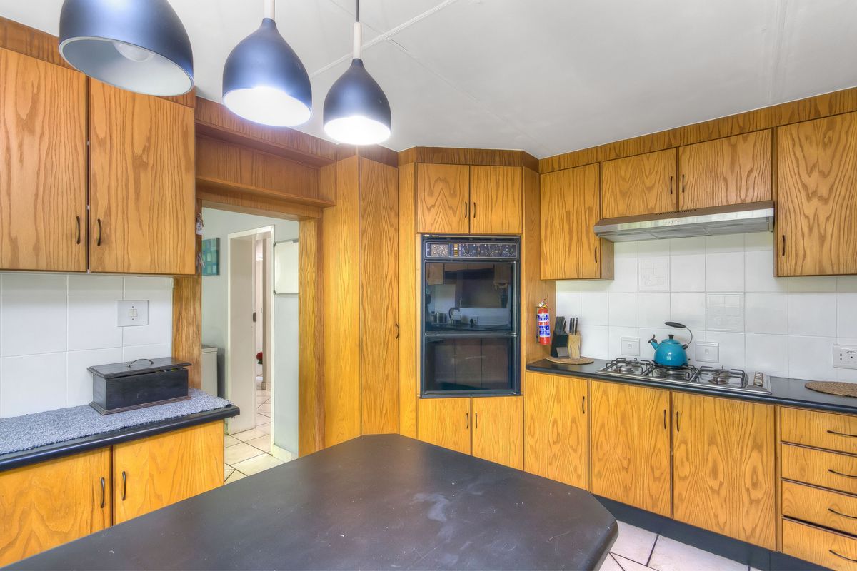 A functional kitchen featuring wood-grain cabinetry, a built-in oven, gas hob, extractor fan, and tiled splashbacks with a central island workspace.