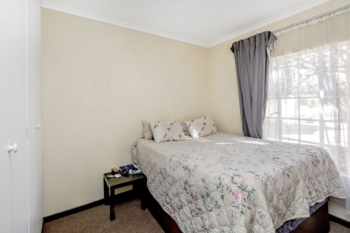 A functional bedroom featuring built-in wardrobe storage, carpeted flooring, and a large window allowing natural light.