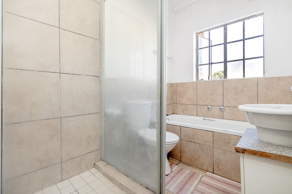 A functional bathroom featuring a shower enclosure, a built-in bathtub, and a pedestal sink with tiled walls and a window for natural light.