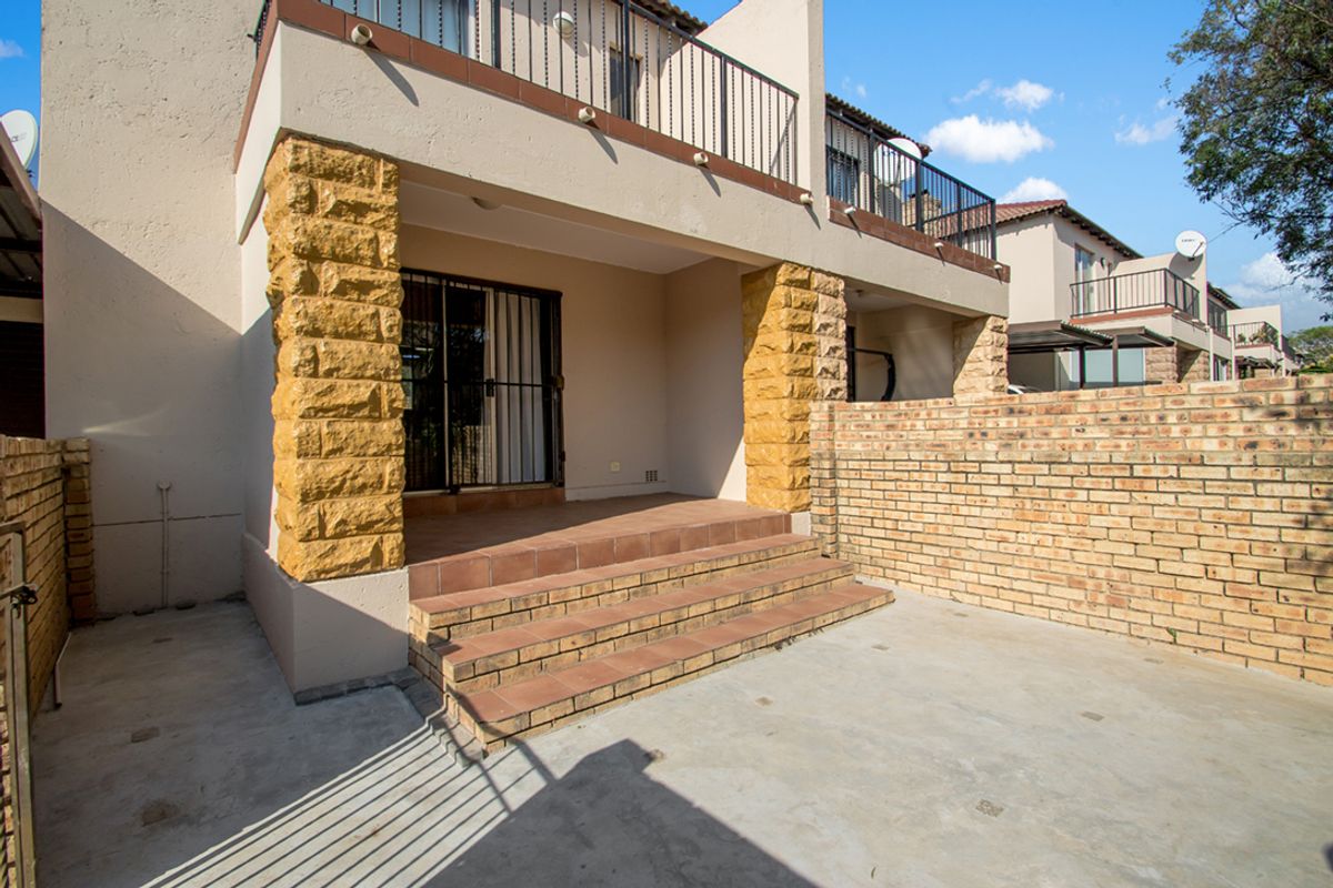 A rear patio area featuring stone-clad pillars, tiled steps, and a brick boundary wall, providing access to the townhouse interior via sliding doors.
