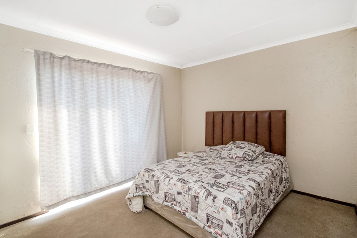 A standard bedroom featuring neutral wall finishes, carpeted flooring, and a large window with curtain coverage.