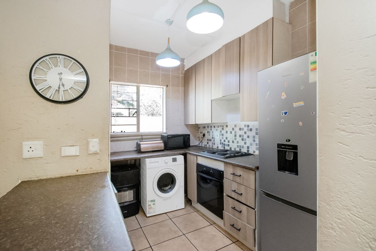 Compact kitchen featuring light wood cabinetry, built-in oven, hob, extractor fan, and tiled flooring with space for laundry appliances.