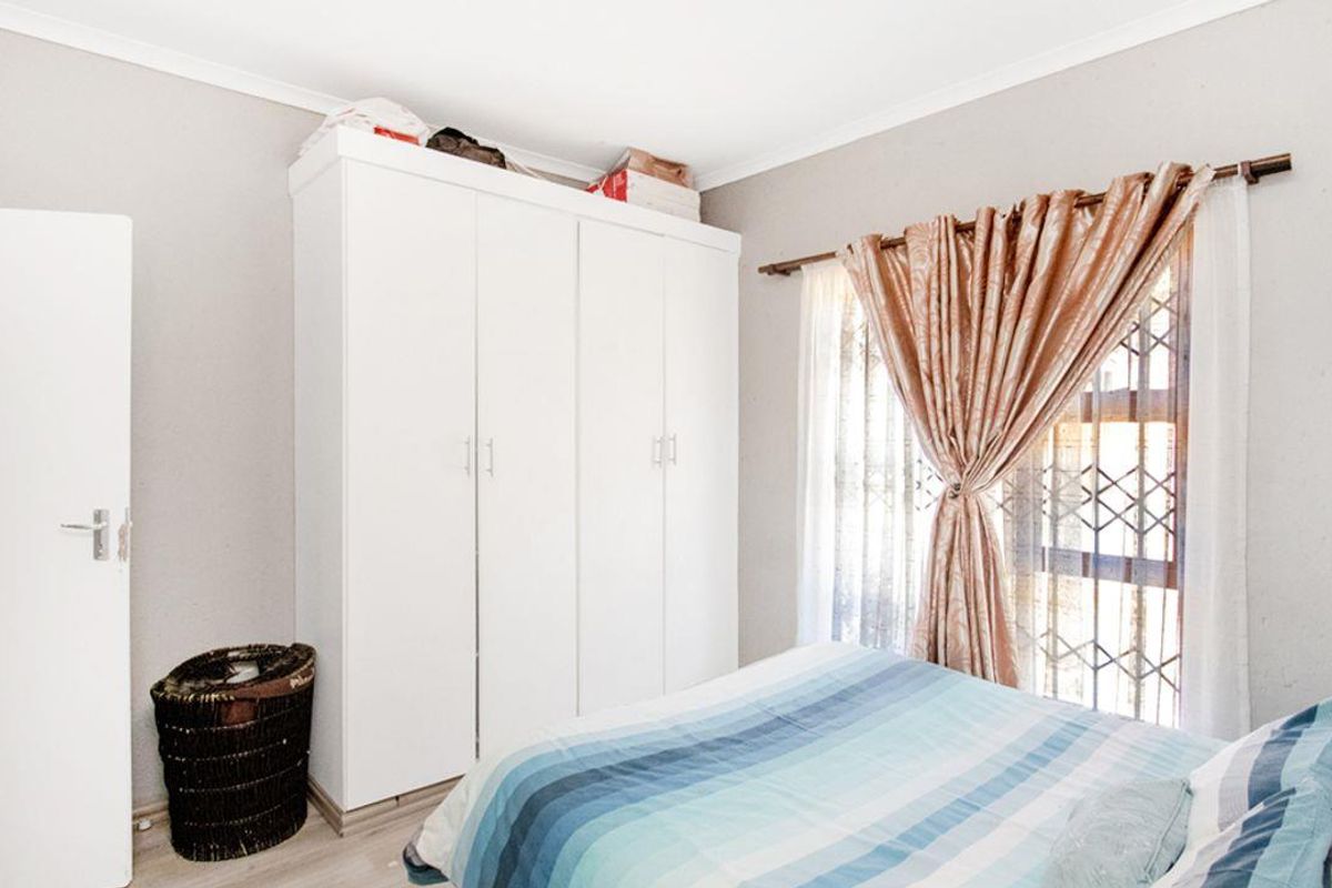 A bedroom featuring built-in white cabinetry and a window fitted with security bars.