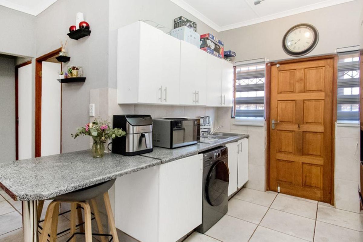 A functional kitchen featuring white cabinetry, granite-look countertops, tiled flooring, and a built-in sink, with direct access to an exterior wooden door.