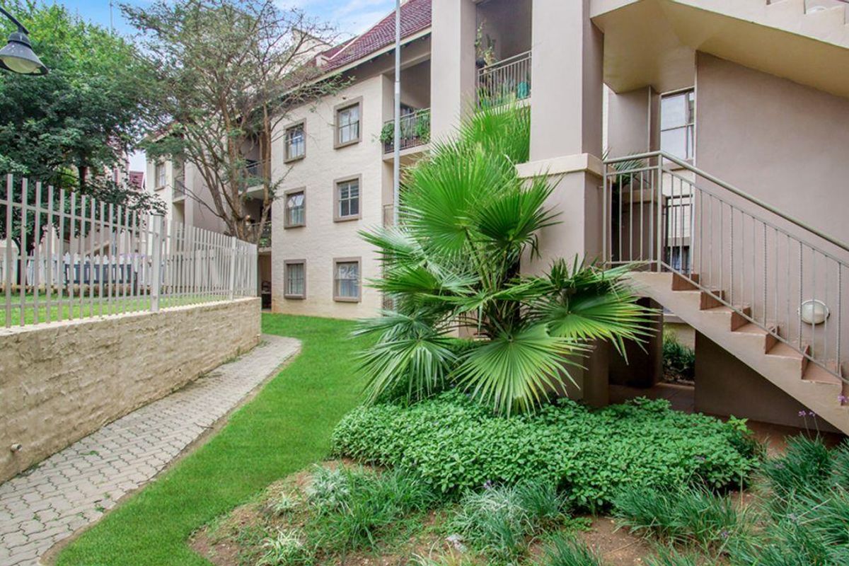 Exterior view of the apartment complex featuring landscaped garden areas, paved walkways, and external staircases leading to upper-level units.