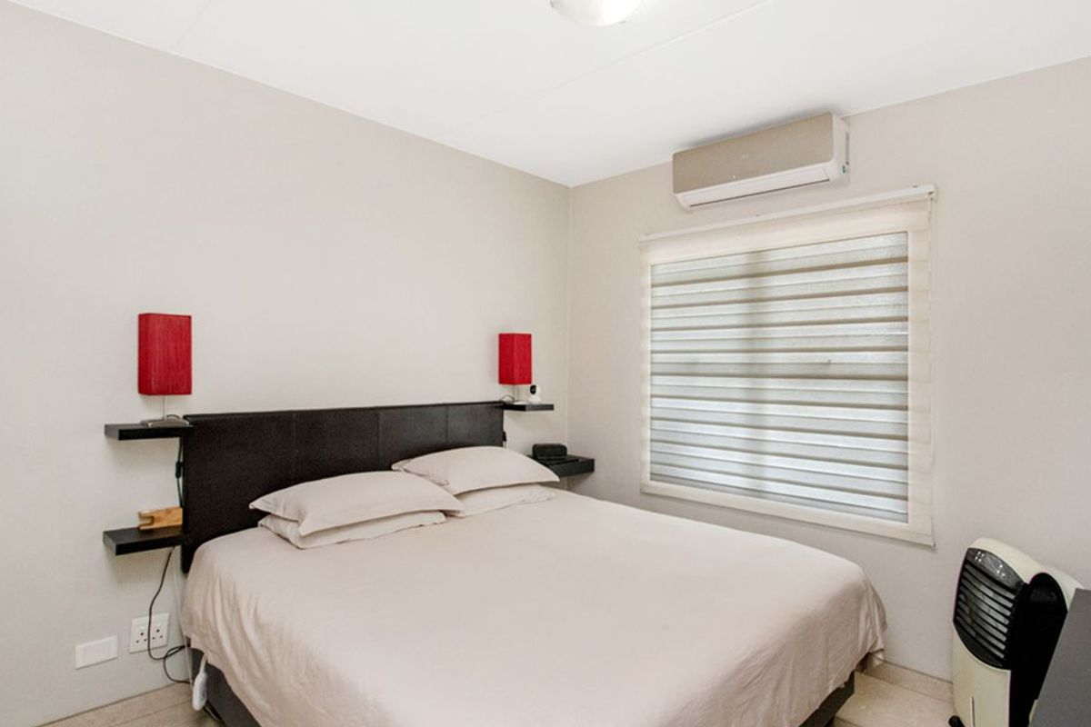 A well-maintained bedroom featuring a wall-mounted air conditioning unit, neutral wall finishes, and fitted window blinds.