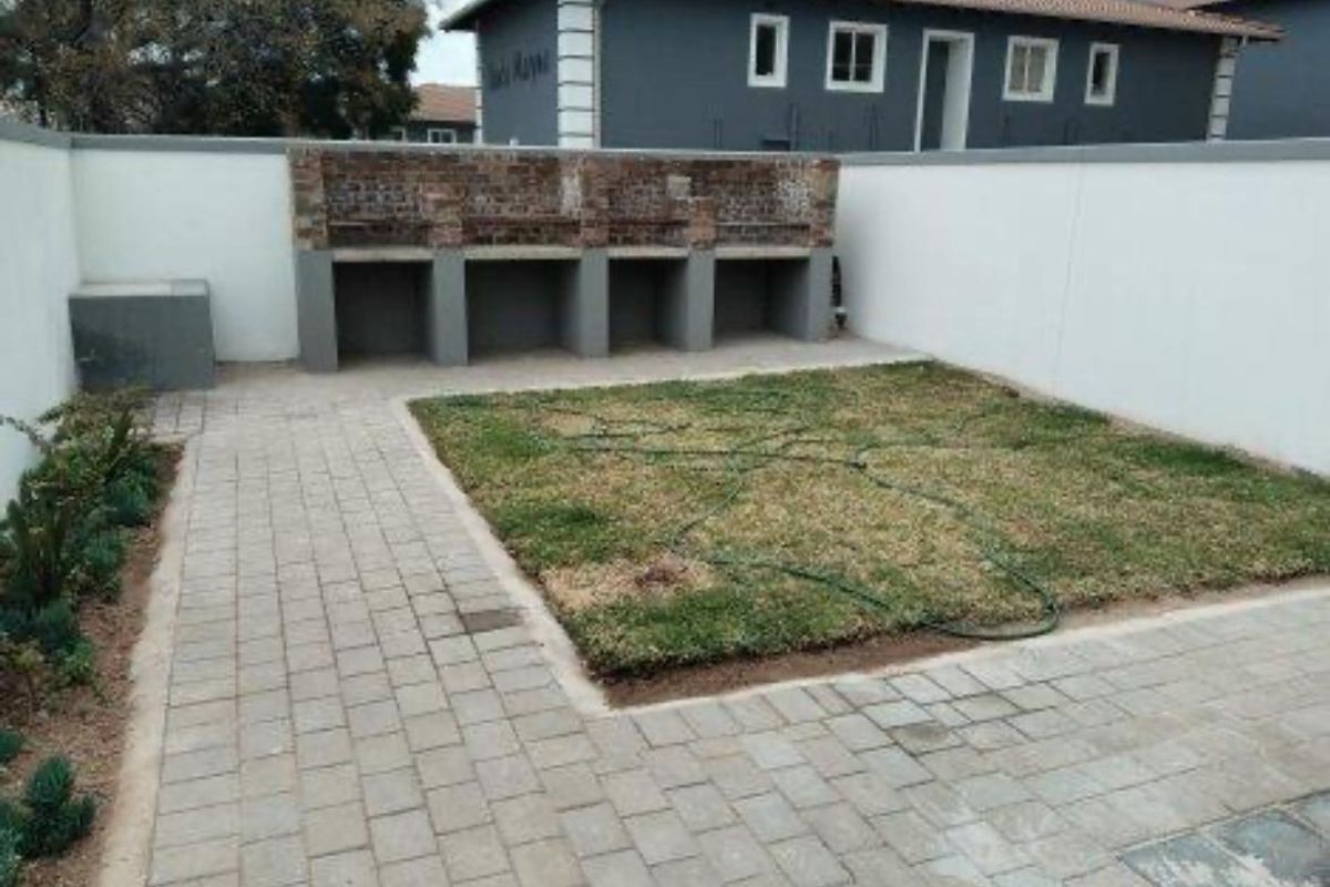 A private rear courtyard featuring a paved patio area, a built-in brick braai, and a small lawn enclosed by boundary walls.