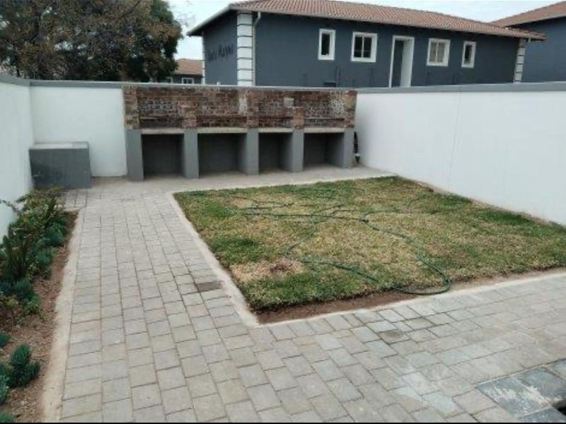 A private rear courtyard featuring a paved patio area, a built-in brick braai, and a small lawn enclosed by boundary walls.