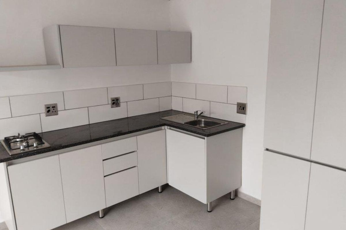 A modern, clean kitchen featuring white cabinetry, dark granite countertops, a gas hob, and a subway tile backsplash in a neutral, minimalist setting.