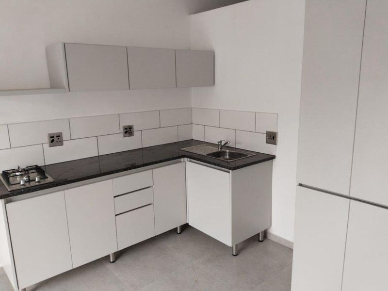A modern, clean kitchen featuring white cabinetry, dark granite countertops, a gas hob, and a subway tile backsplash in a neutral, minimalist setting.