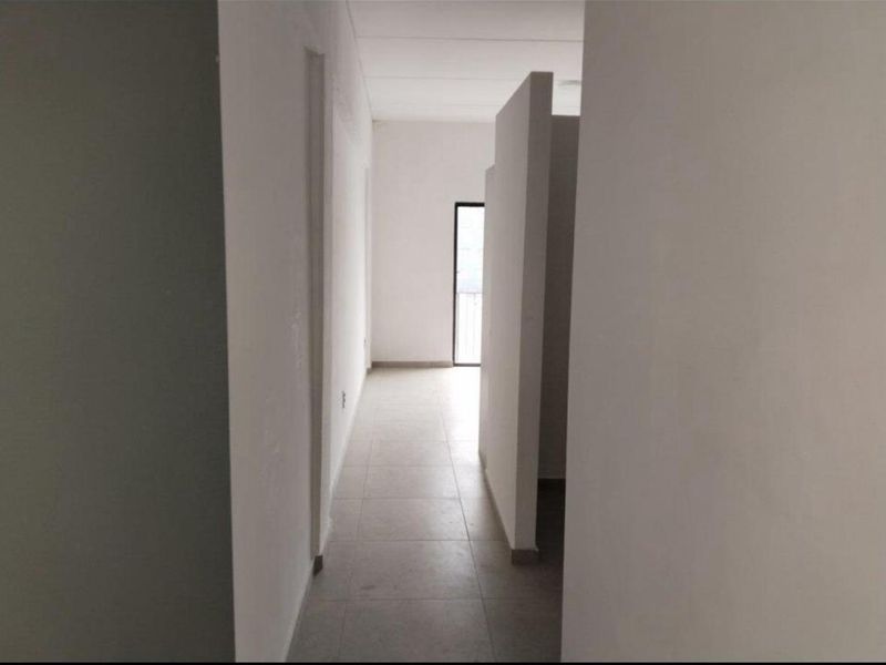 A minimalist, empty hallway featuring neutral tiled flooring and a structural partition wall leading towards a bright doorway.