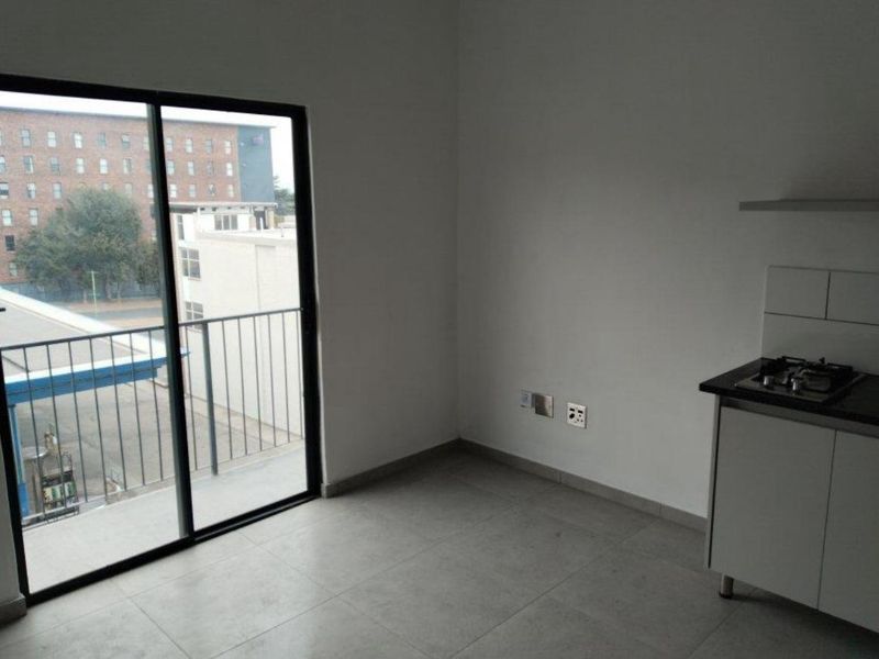 An open-plan living and kitchen area featuring tiled floors, a built-in gas hob, and a sliding glass door leading to a balcony.
