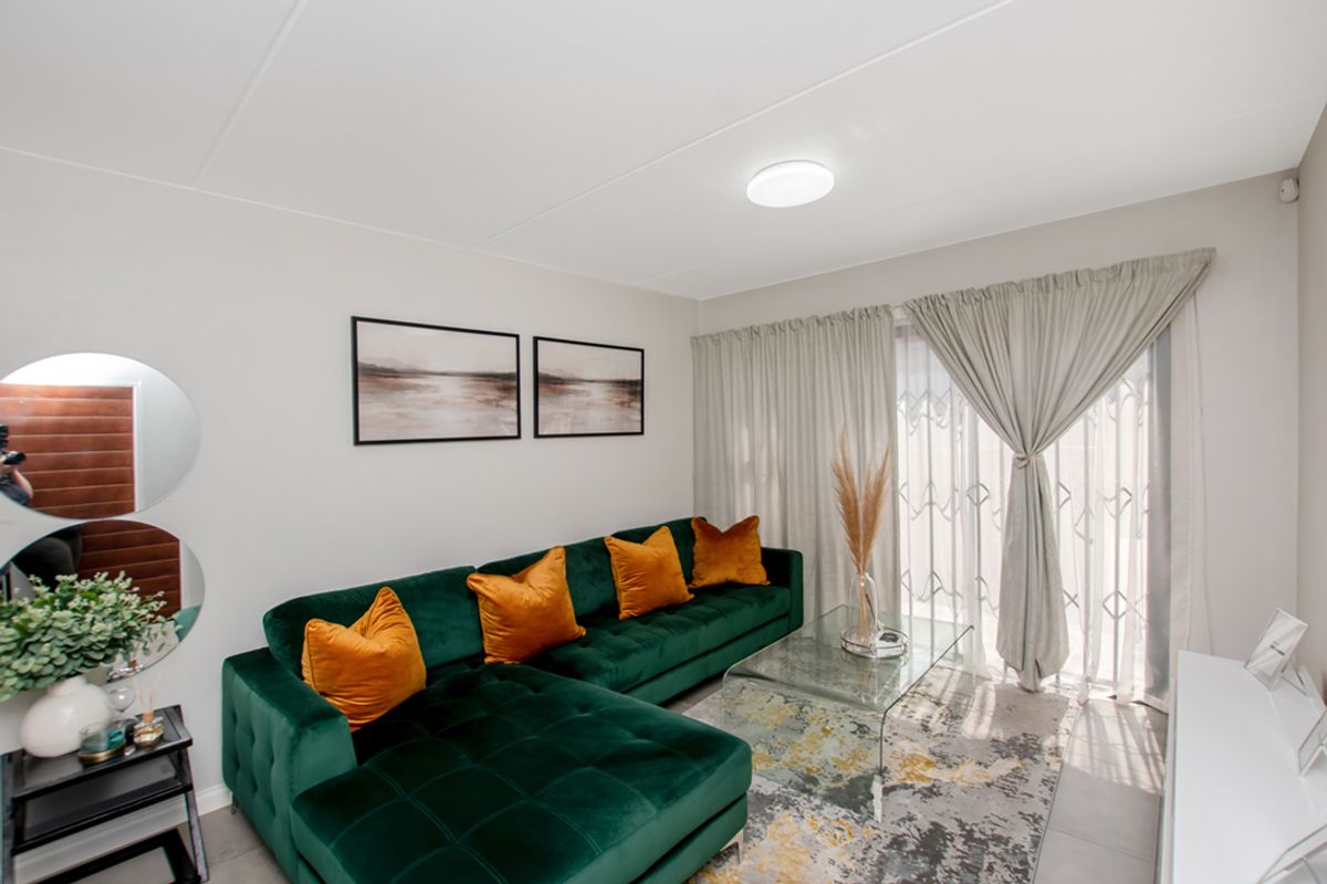 A bright and well-maintained living room featuring tiled flooring and a sliding glass door with security gate, providing access to the outdoor area.
