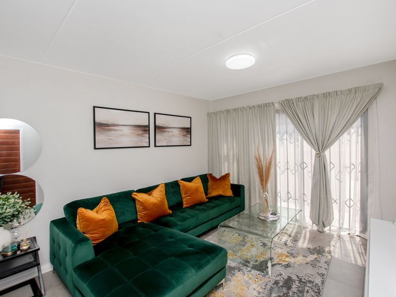 A bright and well-maintained living room featuring tiled flooring and a sliding glass door with security gate, providing access to the outdoor area.