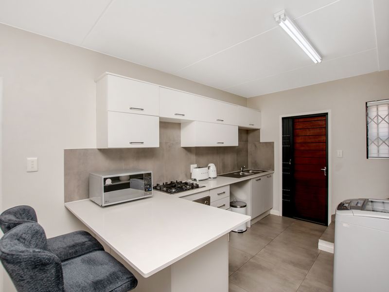 A functional kitchen featuring white built-in cabinetry, a gas hob, tiled backsplash, and neutral floor tiles, providing a clean and practical cooking space.
