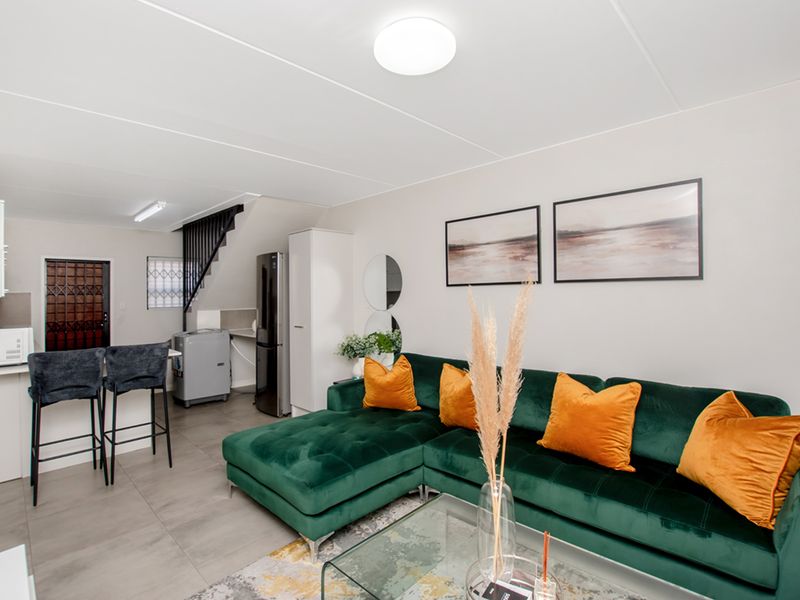 Open-plan living area featuring tiled flooring, a breakfast bar, and a staircase with a modern metal balustrade, creating a functional and connected living space.