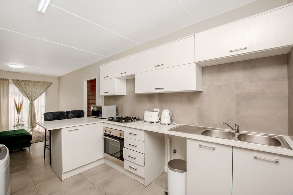 Modern kitchen featuring white cabinetry, gas hob, built-in oven, stainless steel sink, and neutral tiled splashback, seamlessly flowing into the adjacent living area.