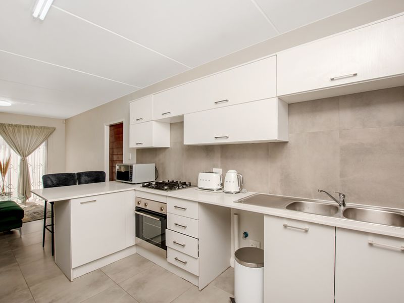 Modern kitchen featuring white cabinetry, gas hob, built-in oven, stainless steel sink, and neutral tiled splashback, seamlessly flowing into the adjacent living area.